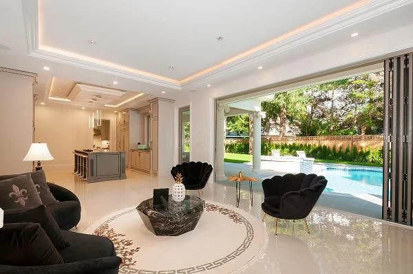 Luxury living space designed and built by True Vision Construction — open bi-fold doors to pool and garden with designer furniture and marble floor medallion