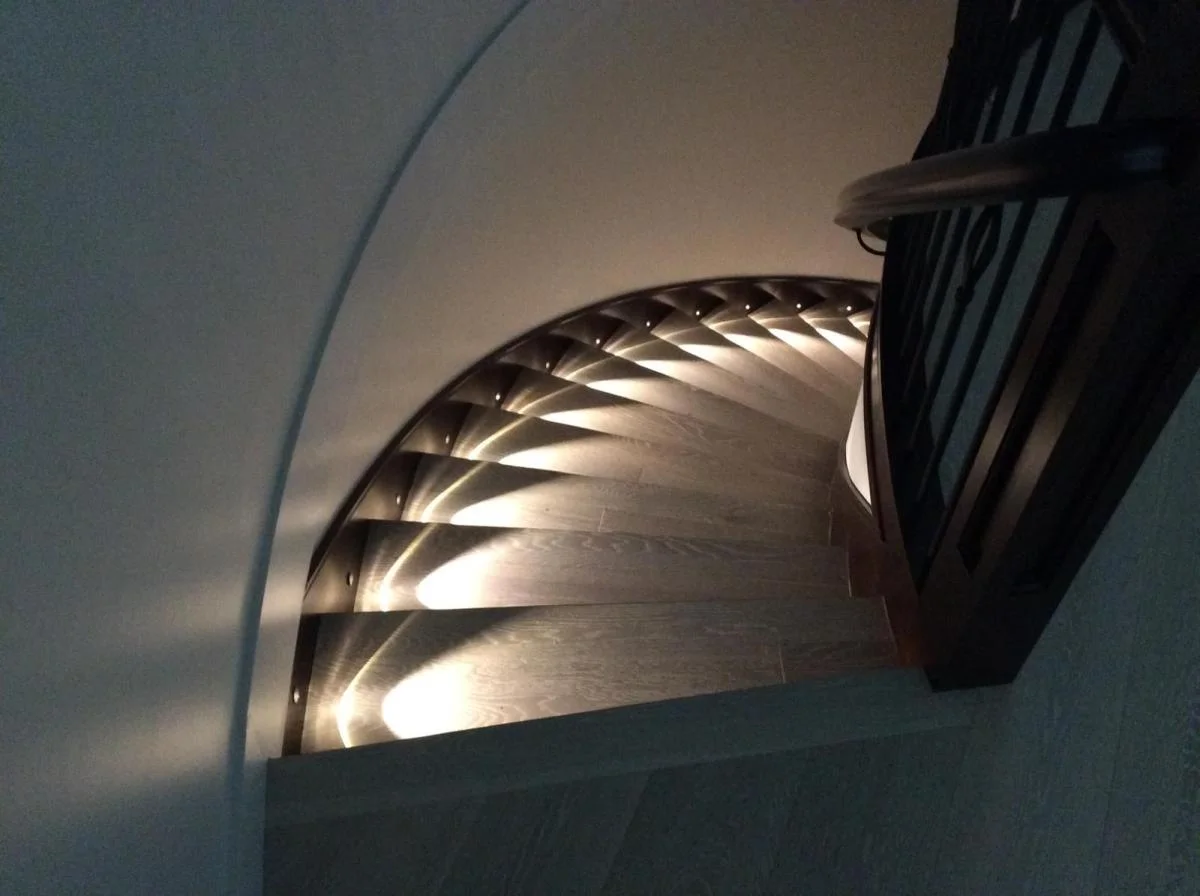 Custom spiral staircase with LED step lighting and wrought iron railing — North Vancouver home builder
