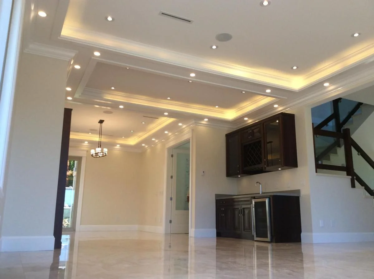 Open-plan interior with coffered LED ceiling, custom cabinetry, and glass staircase during construction